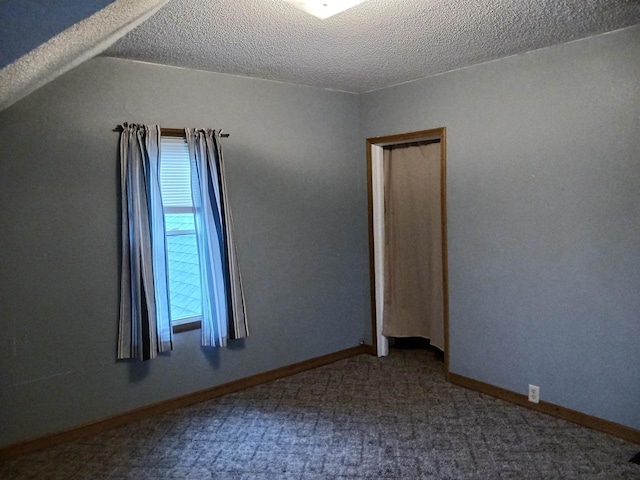 carpeted empty room featuring baseboards, vaulted ceiling, and a textured ceiling