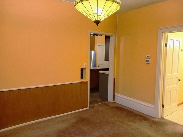 carpeted empty room featuring wainscoting and wooden walls