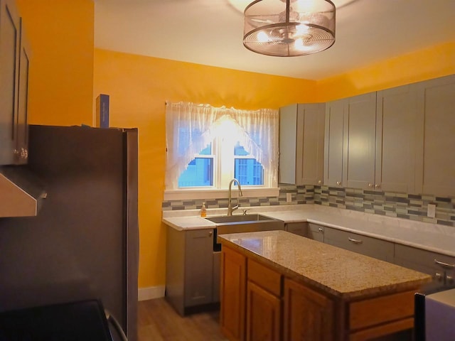 kitchen with decorative backsplash, brown cabinets, freestanding refrigerator, light stone countertops, and a sink