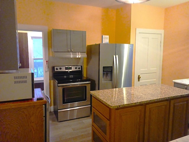 kitchen with light stone counters, under cabinet range hood, stainless steel appliances, light wood finished floors, and brown cabinetry