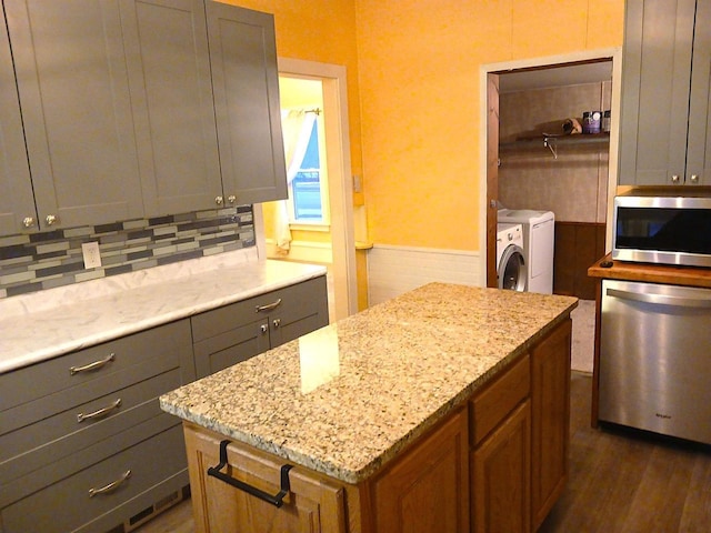 kitchen with light stone counters, washing machine and dryer, a kitchen island, appliances with stainless steel finishes, and brown cabinets