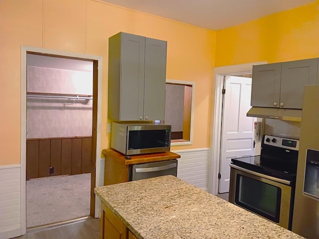 kitchen with a wainscoted wall, appliances with stainless steel finishes, gray cabinets, and under cabinet range hood