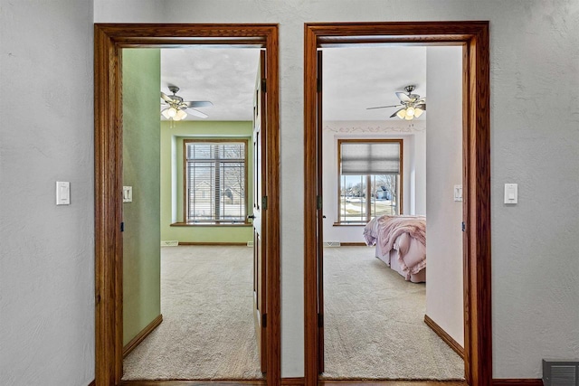 hall with baseboards, carpet flooring, visible vents, and a healthy amount of sunlight