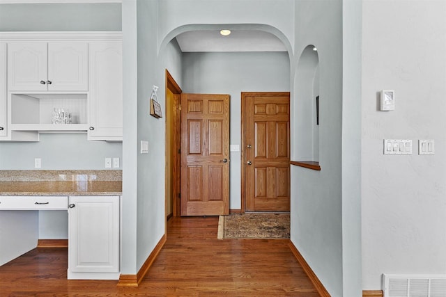 hall with dark wood-type flooring, arched walkways, visible vents, and baseboards