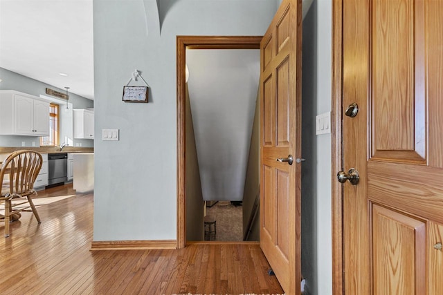 hallway with light wood-style floors, a sink, and baseboards