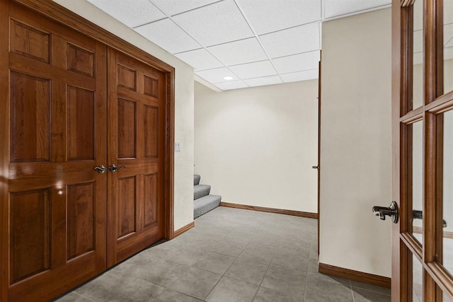 corridor with baseboards, stairway, and a drop ceiling