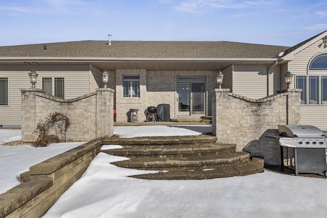 snow covered property entrance featuring a shingled roof