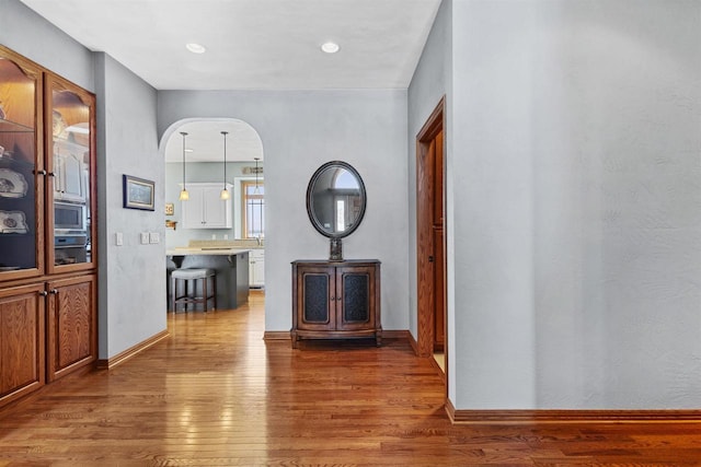 hallway with arched walkways, recessed lighting, baseboards, and wood finished floors