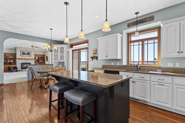 kitchen featuring a fireplace, a kitchen island, a sink, white cabinets, and open floor plan