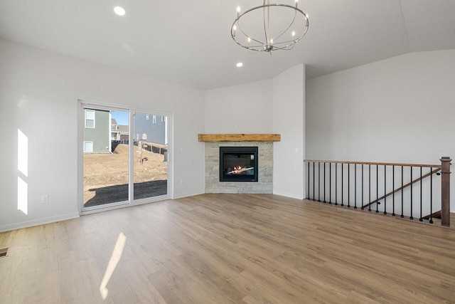 unfurnished living room featuring a notable chandelier, recessed lighting, light wood-style floors, vaulted ceiling, and a glass covered fireplace