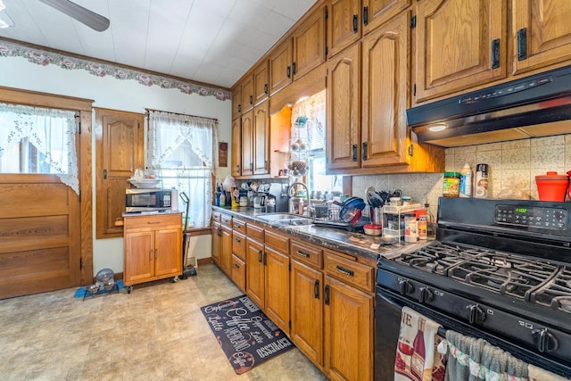 kitchen with brown cabinetry, dark countertops, black gas stove, under cabinet range hood, and a sink