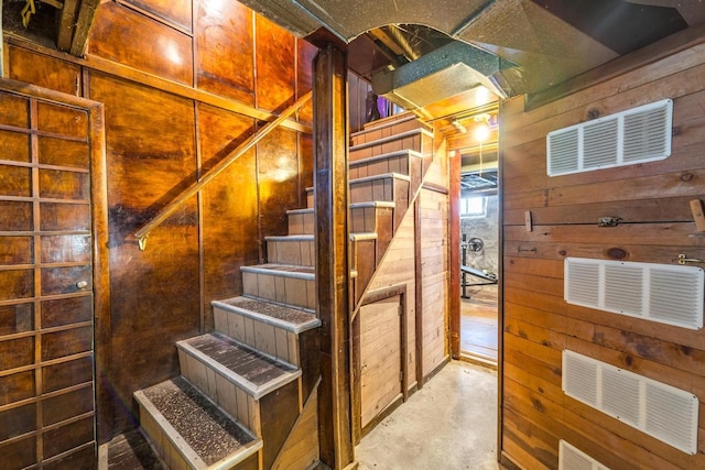 stairway with wood walls and unfinished concrete floors