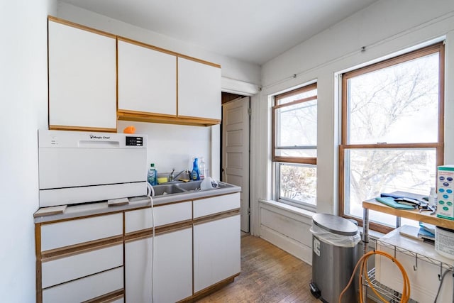 kitchen with light wood-type flooring, a sink, and white cabinetry