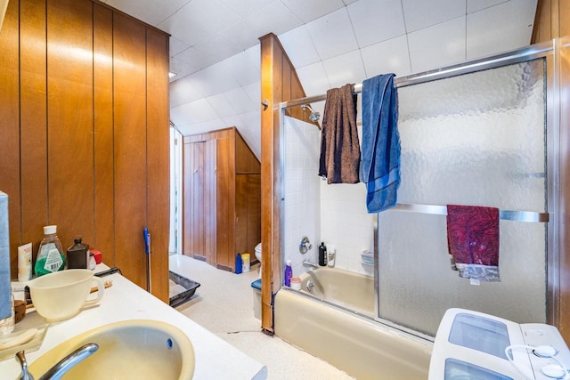 full bathroom with toilet, wood walls, a sink, combined bath / shower with glass door, and washer / clothes dryer