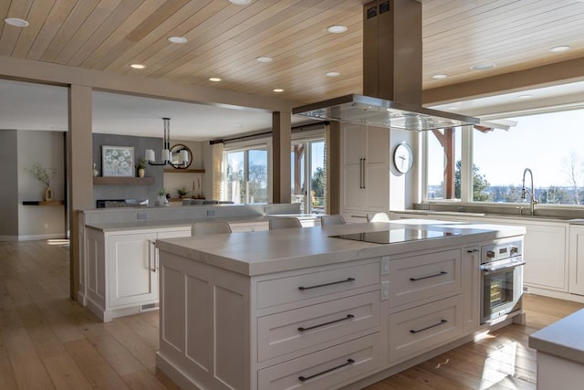 kitchen featuring island exhaust hood, white cabinetry, stainless steel oven, a sink, and a kitchen island