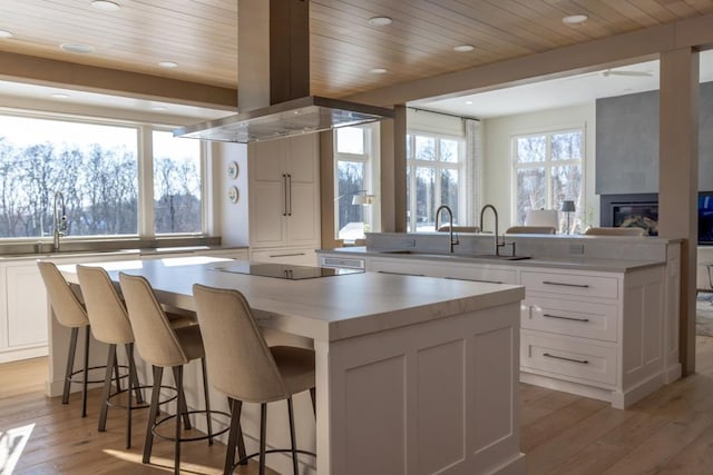 kitchen with white cabinets, a large island, a peninsula, island exhaust hood, and black electric cooktop