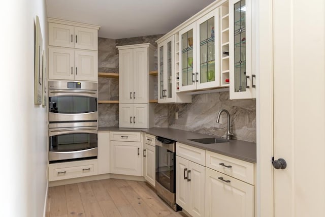 kitchen featuring dark countertops, glass insert cabinets, double oven, a sink, and beverage cooler