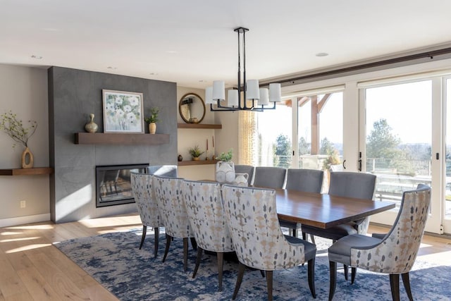 dining room with a large fireplace, a chandelier, light wood-style flooring, and baseboards