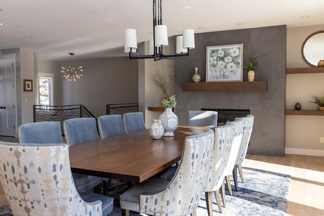 dining area featuring light wood-style floors, baseboards, a fireplace, and a chandelier