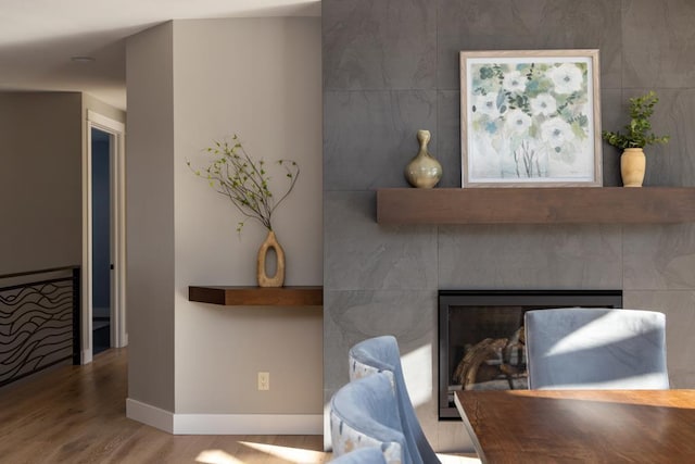 interior space with a glass covered fireplace, baseboards, and wood finished floors