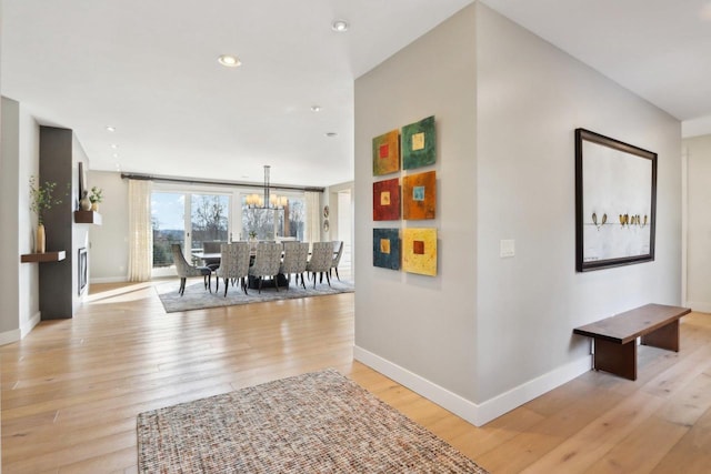 corridor with a chandelier, recessed lighting, light wood-style flooring, and baseboards