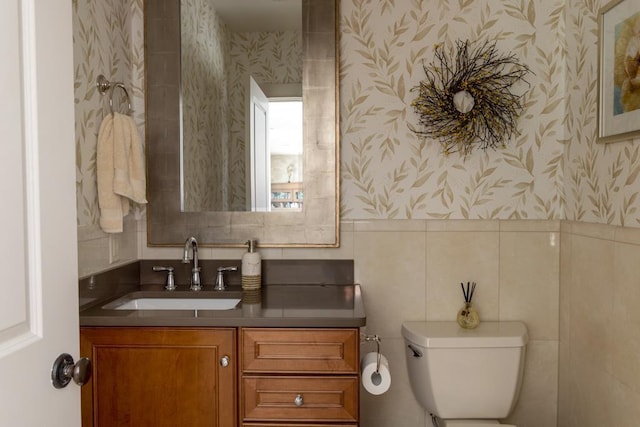 half bathroom with toilet, wallpapered walls, and vanity