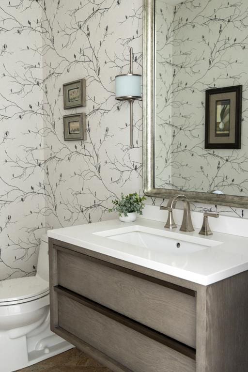 half bath with vanity, toilet, and wallpapered walls