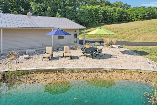 rear view of house with a standing seam roof, metal roof, a patio, a lawn, and a chimney