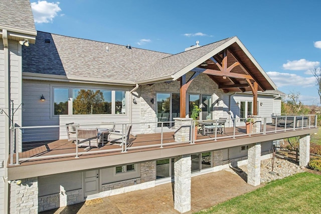 rear view of house featuring stone siding, outdoor dining area, roof with shingles, and a balcony