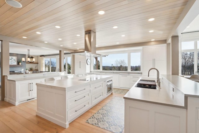 kitchen with light countertops, stainless steel oven, a large island with sink, and island range hood