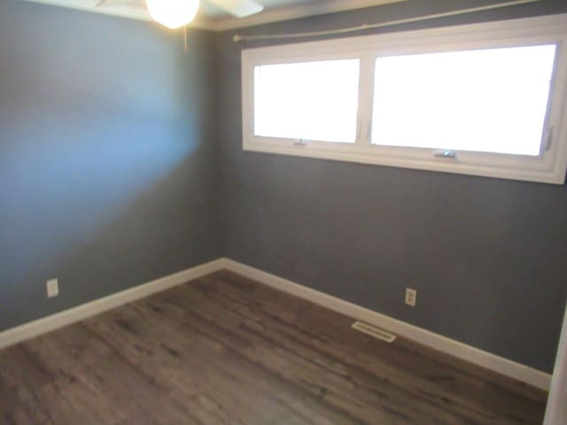 unfurnished room with a ceiling fan, visible vents, baseboards, and dark wood-type flooring