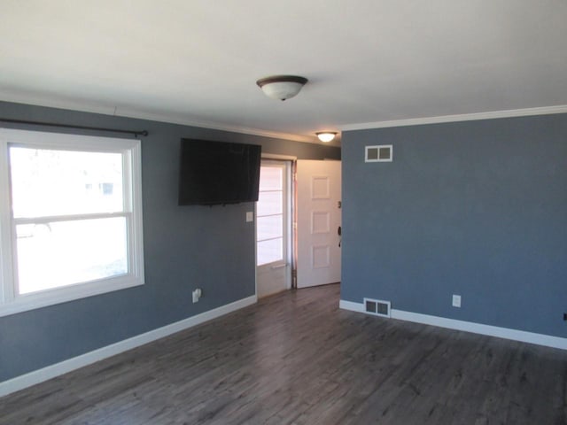 empty room with baseboards, visible vents, dark wood finished floors, and ornamental molding