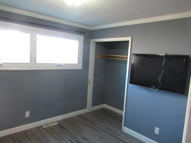 unfurnished bedroom featuring crown molding, a closet, baseboards, and wood finished floors