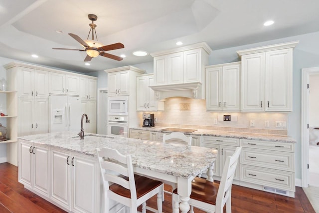 kitchen featuring white appliances, a center island with sink, a breakfast bar, and a sink