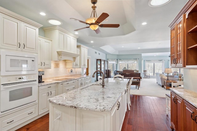 kitchen featuring light stone counters, a kitchen island with sink, white appliances, a sink, and open floor plan