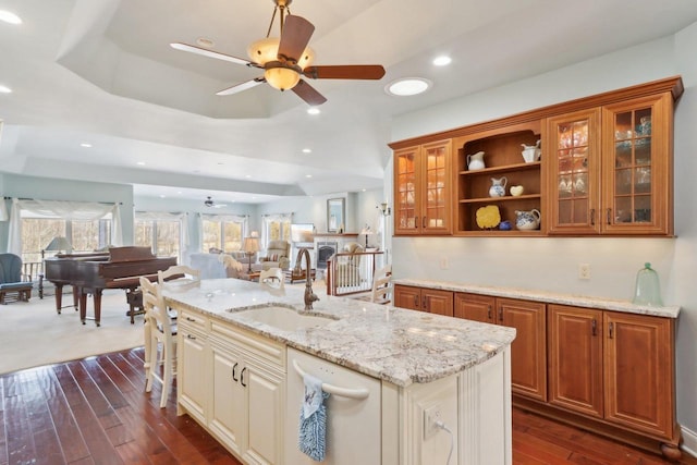 kitchen featuring a center island with sink, brown cabinetry, open floor plan, light stone countertops, and a sink