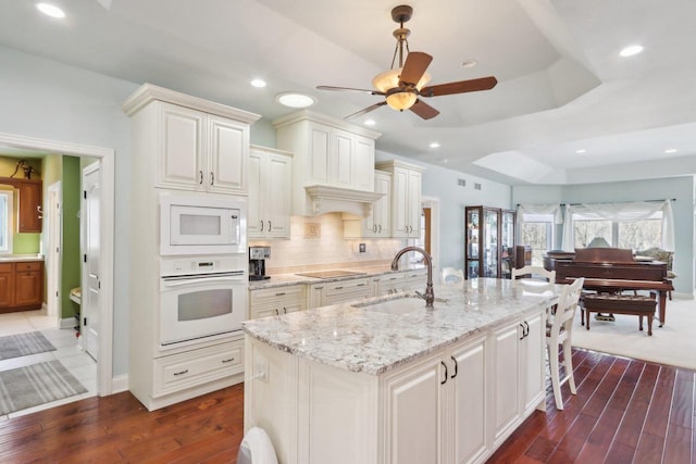 kitchen with light stone counters, white appliances, a sink, tasteful backsplash, and a raised ceiling