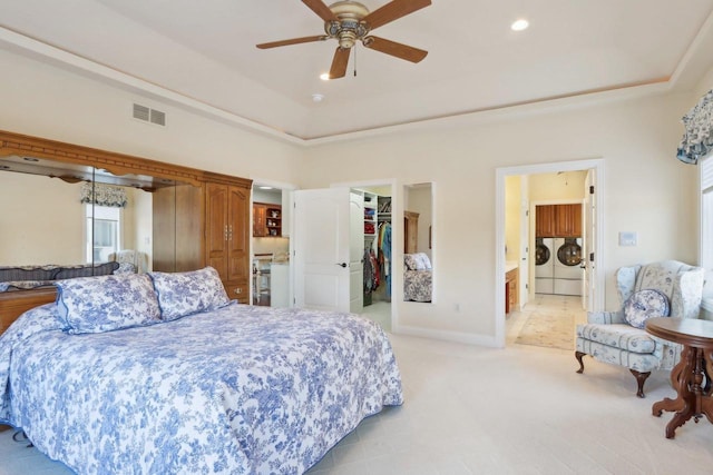 bedroom featuring visible vents, a tray ceiling, washer and dryer, and light colored carpet