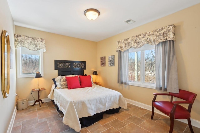 bedroom featuring stone finish floor, baseboards, multiple windows, and visible vents