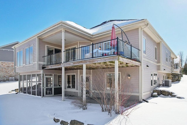 snow covered house with a sunroom, a balcony, and central air condition unit