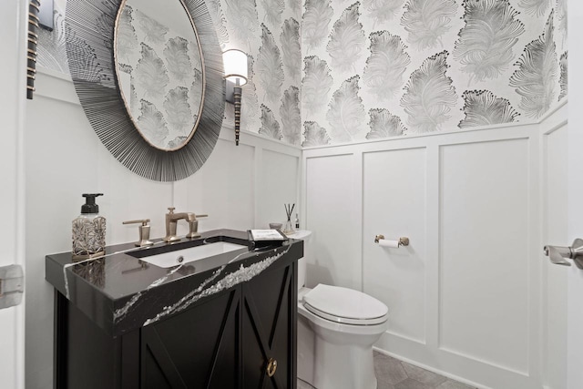 half bath with wainscoting, a decorative wall, vanity, and toilet