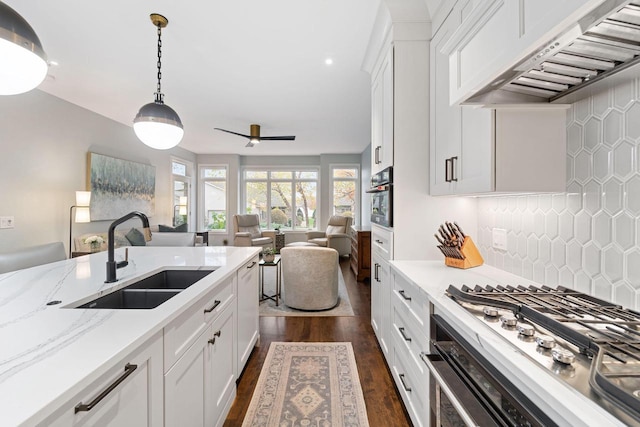 kitchen with open floor plan, white cabinetry, a sink, and wall chimney exhaust hood