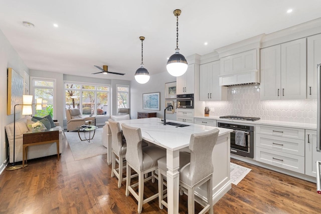 kitchen featuring wall oven, white cabinets, a sink, and an island with sink