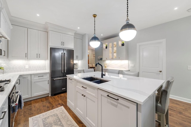 kitchen featuring high quality fridge, a sink, white cabinets, an island with sink, and a kitchen bar