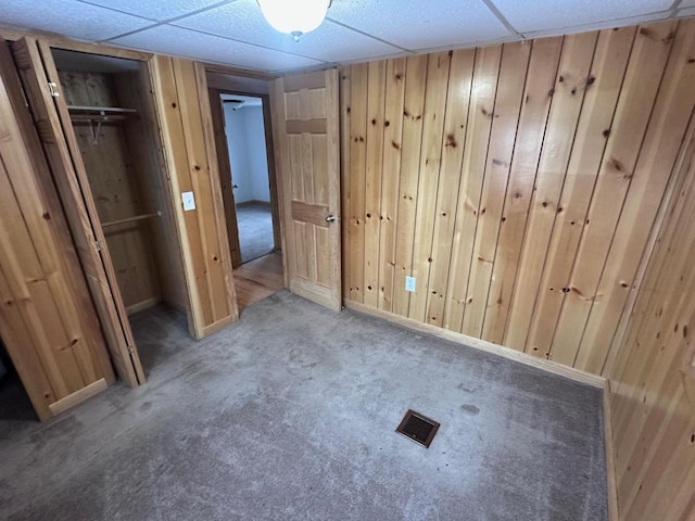 unfurnished bedroom with light carpet, wooden walls, visible vents, and a paneled ceiling