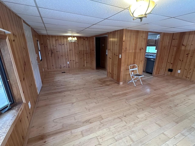 finished basement with a chandelier, wooden walls, a drop ceiling, and light wood-style floors