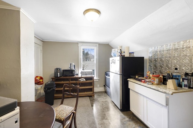 kitchen with light stone counters, lofted ceiling, freestanding refrigerator, white cabinets, and range