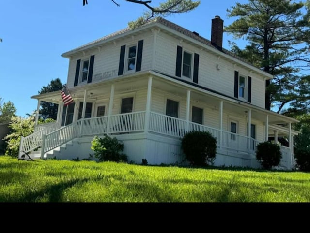 view of front facade featuring covered porch, a chimney, and a front yard