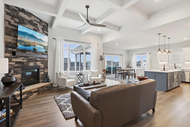 living area featuring beam ceiling, a fireplace, light wood finished floors, ceiling fan, and coffered ceiling