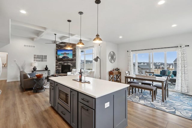 kitchen featuring stainless steel microwave, visible vents, gray cabinetry, light wood-type flooring, and coffered ceiling